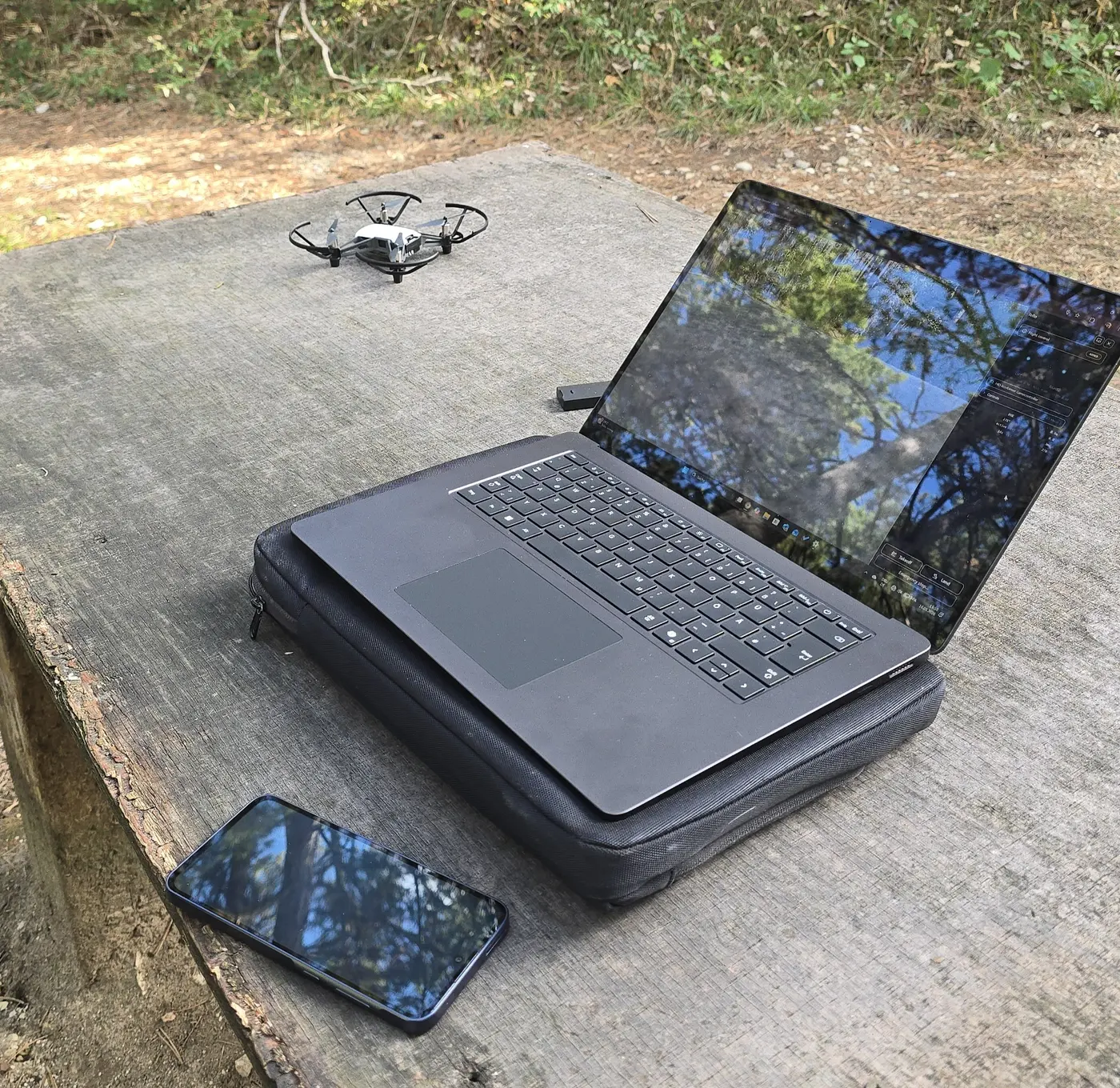 Drohne, Laptop und Handheld-Gerät auf einem Holztisch im Wald